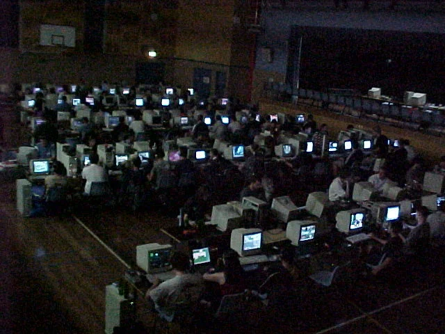 A darkened school hall around 2000, packed with rows of players at beige PCs, the CRT monitors glowing